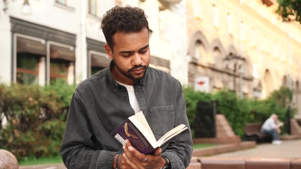 A man reading an open paperback on an old-town street