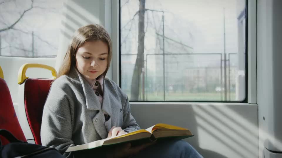 A woman reading a book by the window of a tram