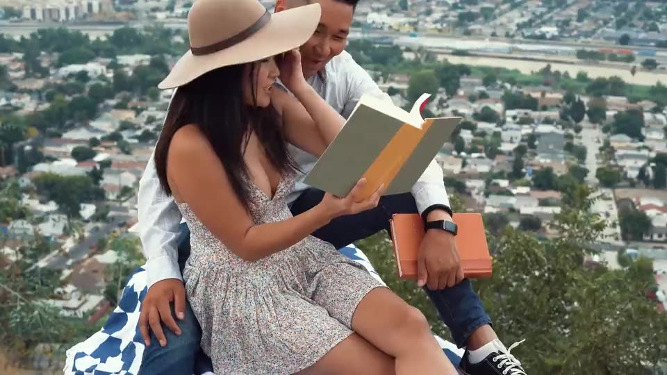 A couple sharing a book on a hillside above a city